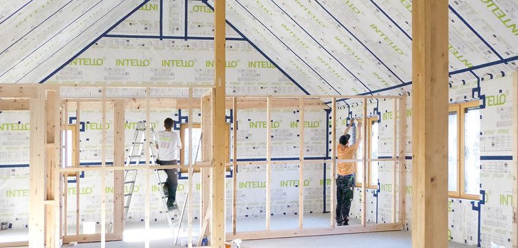 Two tradespeople installing INTELLO membranes inside the roof and walls of a bright house.